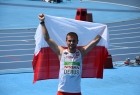 mężczyna w białej koszulce reprezentacji Polski stoi z rękami uniesionymi do góry, trzymając biało-czerwona flagę