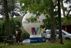 Zza drzew widać balon pneumatyczny z napisem Małopolska i samochód. W tle dwoje uczestników