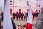 Grupa osób stojących przed pomnikiem w Brzesku podczas symbolicznej uroczystości