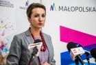 Marta Malec-Lech z zarządu województwa podczas konferencji prasowej stoi przed mikrofonami; w tle roll-upy Małopolski i Bibilioteki w Tarnowie