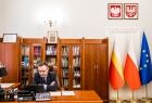 Wicemarszałek Tomasz Urynowicz w swoim gabinecie, w tle szafa i trzy flagi