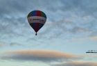 Balon z logo Małopolski unoszący się na tle szaro-granatowego, zachmurzonego nieba nad łagodnymi stokami Sudetów