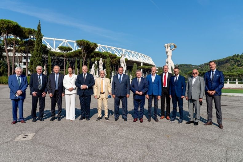 Wspólne pamiątkowe zdjęcie uczestników spotkania w Rzymie ws. organizacji III Igrzysk Europejskich. Kilkanaście osób stoi obok siebie na osłonecznionym placu, na tle błękitniego nieba