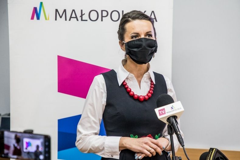 Marta Malec-Lech z zarządu województwa mówi do mikrofonu. W tle widoczna ścianka z logo i napisem Małopolska.