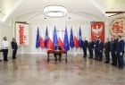 Prezydent podpisuje ustawę, obok goście wydarzenia, w tle flagi Polski i UE