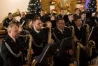 Orkiestra OSP Męcina koncertuje w kościele. W tle widoczne ubrane w światełka choinki.