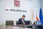 Wicemarszałek Łukasz Smółka podpisuje dokument. Za nim na ścianie godło Małopolski i napis Małopolska. Obok flagi Małopolski, Polski i Unii Europejskiej.