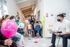 Wicemarszałek Łukasz Smółka siedzi z dziećmi na szpitalnym korytarzu i czyta im bajki. Na pierwszym planie różowy balon z napisem Małopolska.
