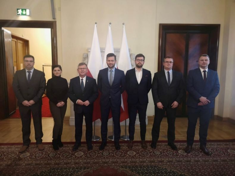 Ministrowie i samorządowcy na spotkaniu w KPRM, na zdjęciu marszałek małopolski. w tle biało-czerwone flagi 