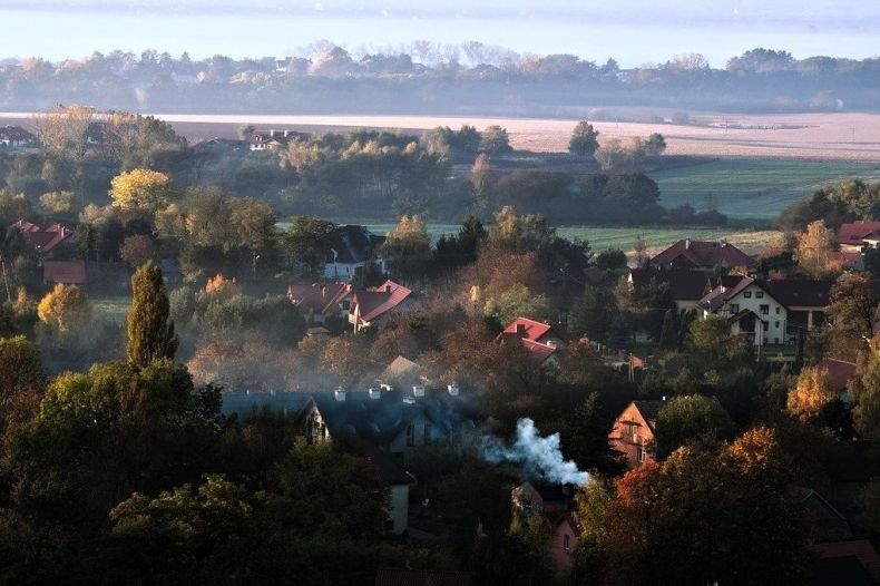 Wieś. Widok z lotu ptaka na domy pośród zieleni i unoszący się nad nimi biały dym