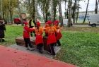 Grupa dzieci w pomarańczowych strojach niesie kubeczki z wodą ustawione na desce