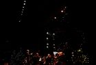 Widok na scenę Opery Krakowskiej na której grają muzycy. Scena jest ciemna, punktowo ciepłym światłem oświetlone są jedynie muzycy. 