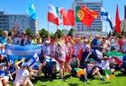 Sportowcy z różnych krajów trzymający flagi pozują do wspólnego zdjęcia na tle zieleni