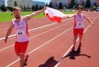 Zawodnicy w biało-czerwonych strojach sportowych biegną przez bieżnię trzymając flagę narodową