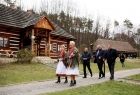 Kilka osób, w tym Iwona Gibas z Zarządu Województwa Małopolskiego ubrana w strój ludowy, idące drogą obok drewnianych chat na terenie Muzeum Nadwiślańskiego Parku Etnograficznego w Wygiełzowie