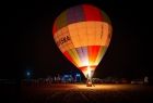 Widok na balon startujący nocą. Balon ma napis MAŁOPOLSKA i kolorowe logo. 