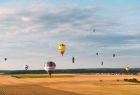 Kolorowe balony unoszą się na błękitnym niebie nad polem zboża