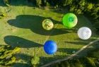 Kilka balonów unosi się nad ziemią, rzucając cień na zieloną polanę