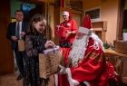 Dziewczynka w czarnej sukience odbiera od Świętego Mikołaja i Marszałka Witolda Kozłowskiego prezent. 