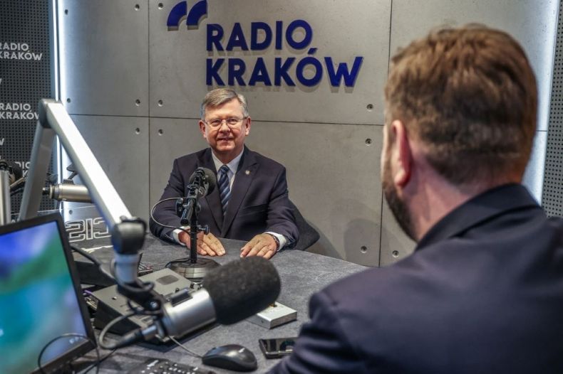 Marszałek Witold Kozłowski siedzi przy stole. Za nim napis Radio Kraków.