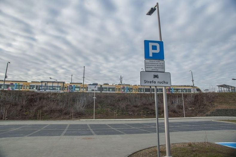 Parking samochodowy, na drugim planie stoi pociąg Kolei Małopolskich.