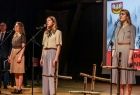 Przedstawienie teatralne w wykonaniu młodych osób - trzy dziewczyny stoją na scenie i mówią do mikrofonu.