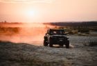 Samochód terenowy jedzie przez pustynię na tle zachodzącego słońca