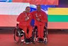 Dwóch reprezentantów Polski na wózkach prezentujący medale. W tle flaga Polski i Litwy. 