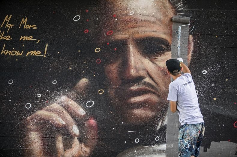 mgr Mors podczas malowania muralu na którym jest głowa i ręka mężczyzny