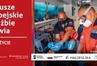 Grafika kampanii: napis Fundusze Europejskie w służbie zdrowia. Ratują życie oraz zdjęcie przedstawiające dwóch ratowników medycznych w maseczkach zaopatruje leżącego na noszach pacjenta
