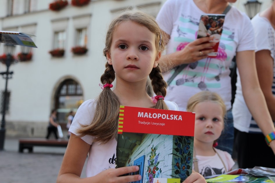 Zdjęcie przedstwia dziewczynkę z publikacją o Małopolsce w ręce