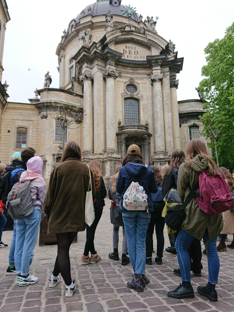 Grupa uczniów stojąca przed wejściem do kościoła, tyłem do obiektywu.