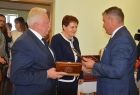 Radny Adam Kwaśniak wręcza dwóm osobom pudełka z medalami.