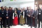 Grupa osób stojących w szeregu. W środku dwie kobiety w strojach ludowych.
