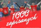 Zdjęcie podzielone na dwie cześci. górna część zdjęcie czwórki biegarzy z podniesionymi dłońmi, poniżej na czerwonym tle napis 1000 zapisanych