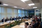 Grupa osób siedząca przy owalnym stole, w tle rząd okien.