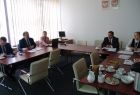 Grupa osób siedzących przy trzech stołach w kształcie litery u. Nad środokowym stołem zawieszone godło Polski i Małopolski.
