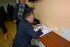 Marszałek Leszek zegzda siedząc wpisuje się do dużej księgi, leżącej przed nim na stole.