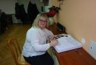 Radna Barbara Dziwisz siedząc wpisuje się do dużej księgi, leżącej przed nią na stole.