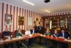 Grupa osób siedząca przy stole w kształcie litery L.