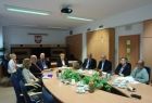 Grupa osób siedząca przy owalnym stole. W tle na ścianie godło województwa.