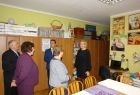 Grupa osób stoi przed ścianą, na której powieszone są prace plastyczne.