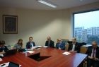 Grupa osób siedzących przy stołach ułożonych w kwadrat. W tle okno.