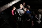 zdjęcie. w ciemnych tonacjach. Wokół dorosłej osoby, która pokazuje coś, skupione są dzieci