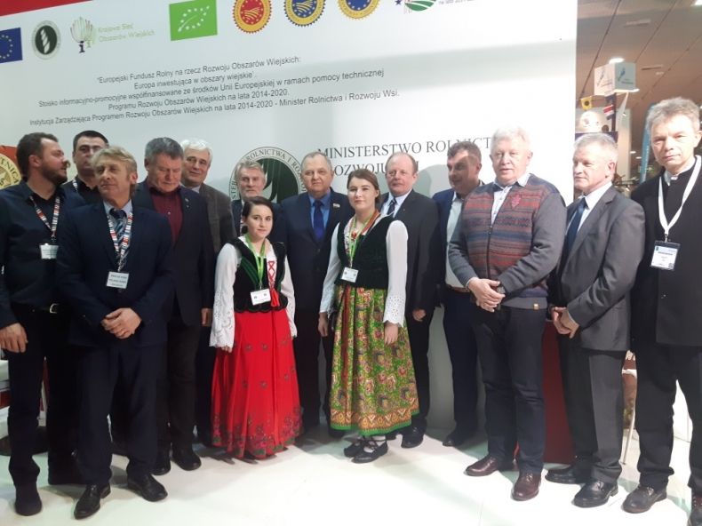 Grupa osób stojących w szeregu. W środku dwie kobiety w strojach ludowych.