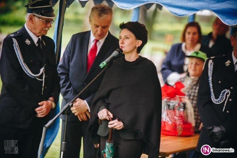 Przewodnicząca Urszula Nowogórska stoi przed mikrofonem w gronie strażaków.