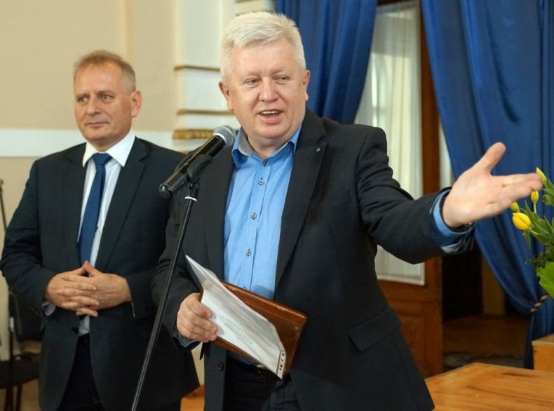 Radni Stanisław Pasoń i Grzegorz Biedroń stoją przy mikrofonie. Stanisław Pasoń trzyma w ręku szkatułkę z medalem.