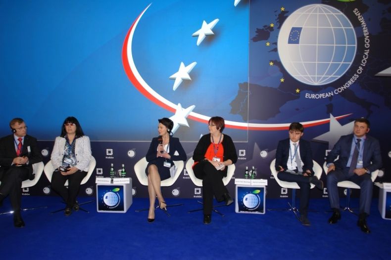 Grupa sześciu osób siedzących na scenie. Trzecia od lewej przewodnicząca sejmiku Urzula Nowogórska z mikrofonem w ręku. W tle logo Europejskiego Kongresu Samorządów.