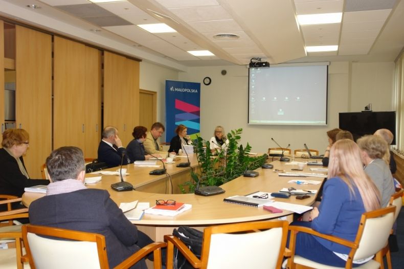 Grupa osób siedzących przy owalnym stole.