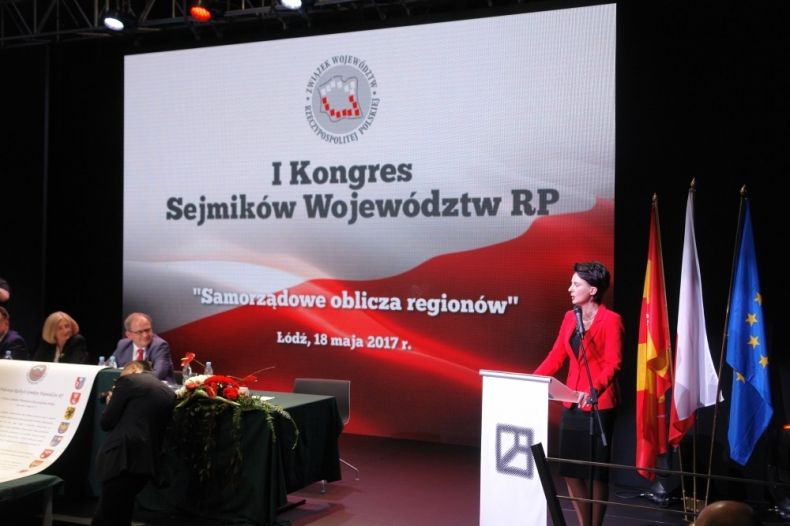 Urszula Nowogórska stoi przy mównicy. Za nią ekran z napisem I Kongres Sejmików Województw RP.